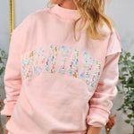 Woman wearing pink oversized mockneck sweatshirt with floral Montana graphic lettering