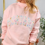 Woman wearing pink oversized mockneck sweatshirt with floral Montana graphic lettering