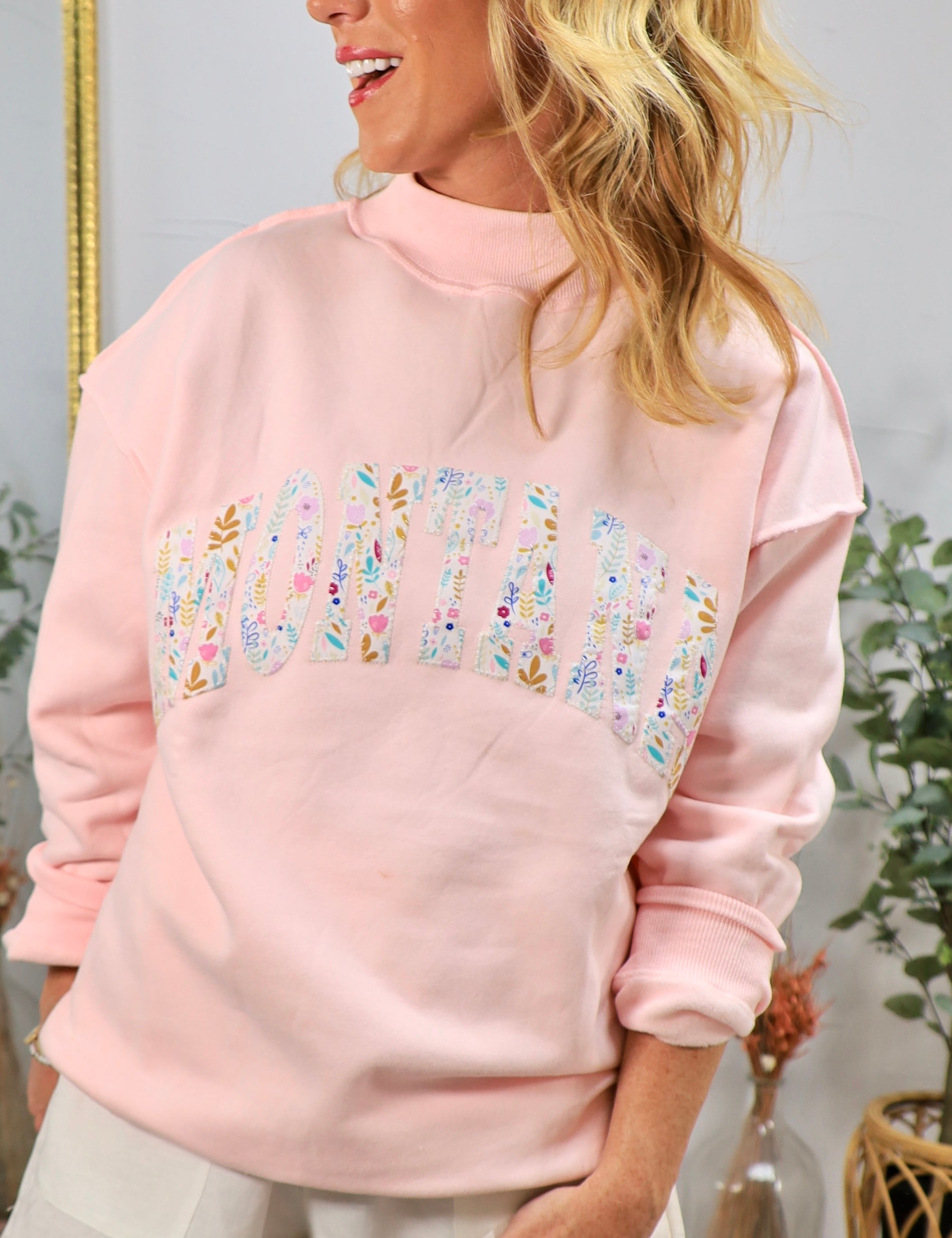 Woman wearing pink oversized mockneck sweatshirt with floral Montana graphic lettering