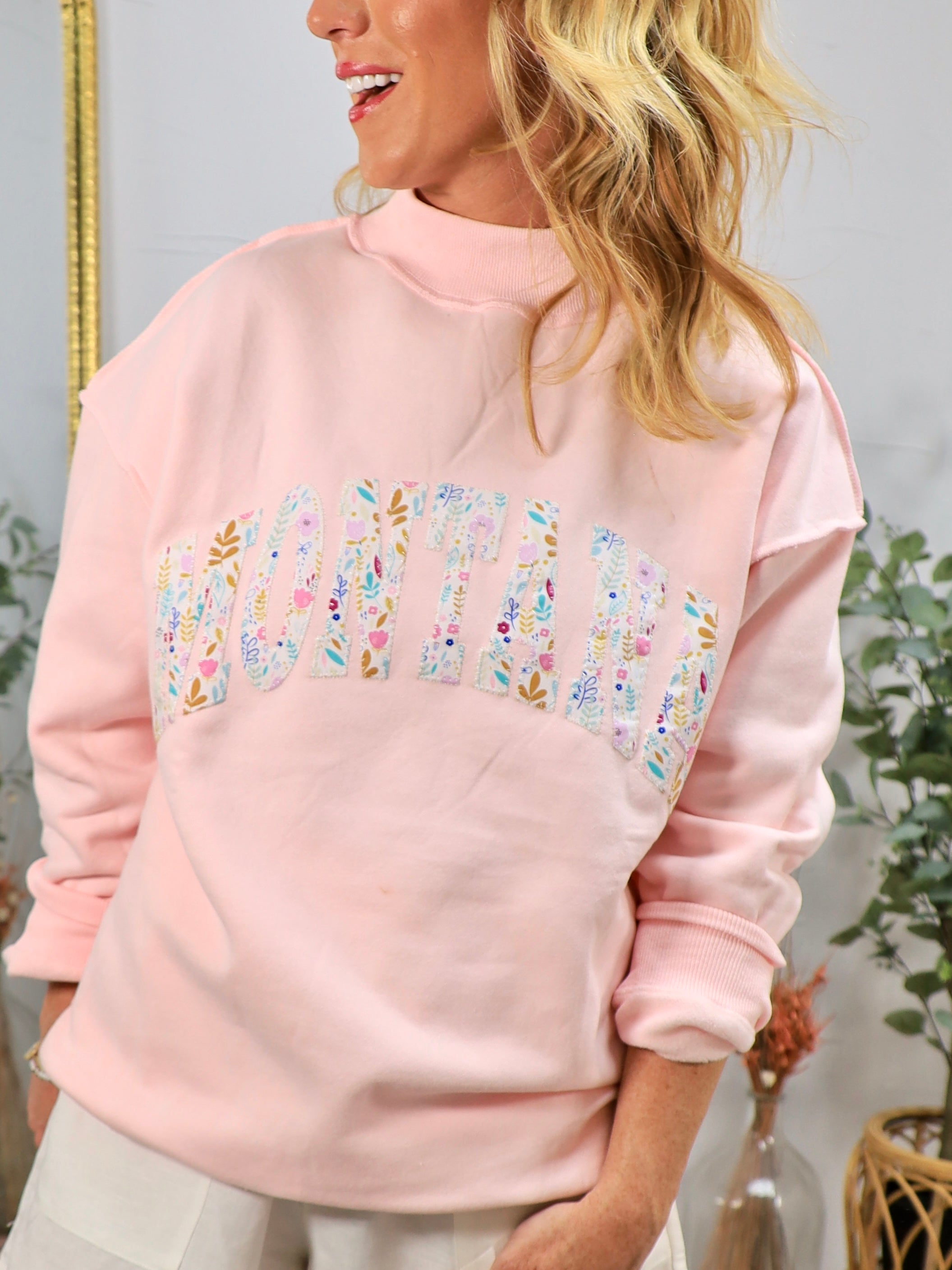 Woman wearing pink oversized mockneck sweatshirt with floral Montana graphic lettering