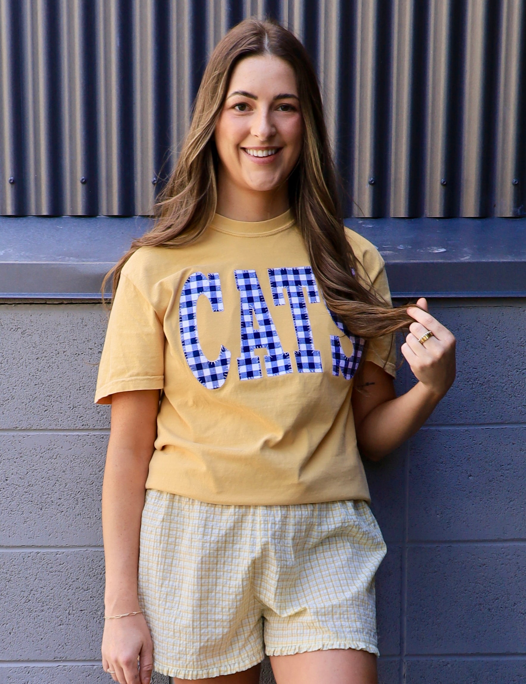 Yellow "CATS" gingham appliqué tee styled with matching plaid smocked shorts, worn by smiling brunette model.