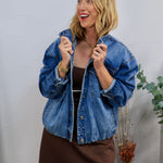 Woman wearing oversized medium wash denim jacket with snap buttons over a brown mini dress