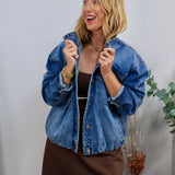 Woman wearing oversized medium wash denim jacket with snap buttons over a brown mini dress