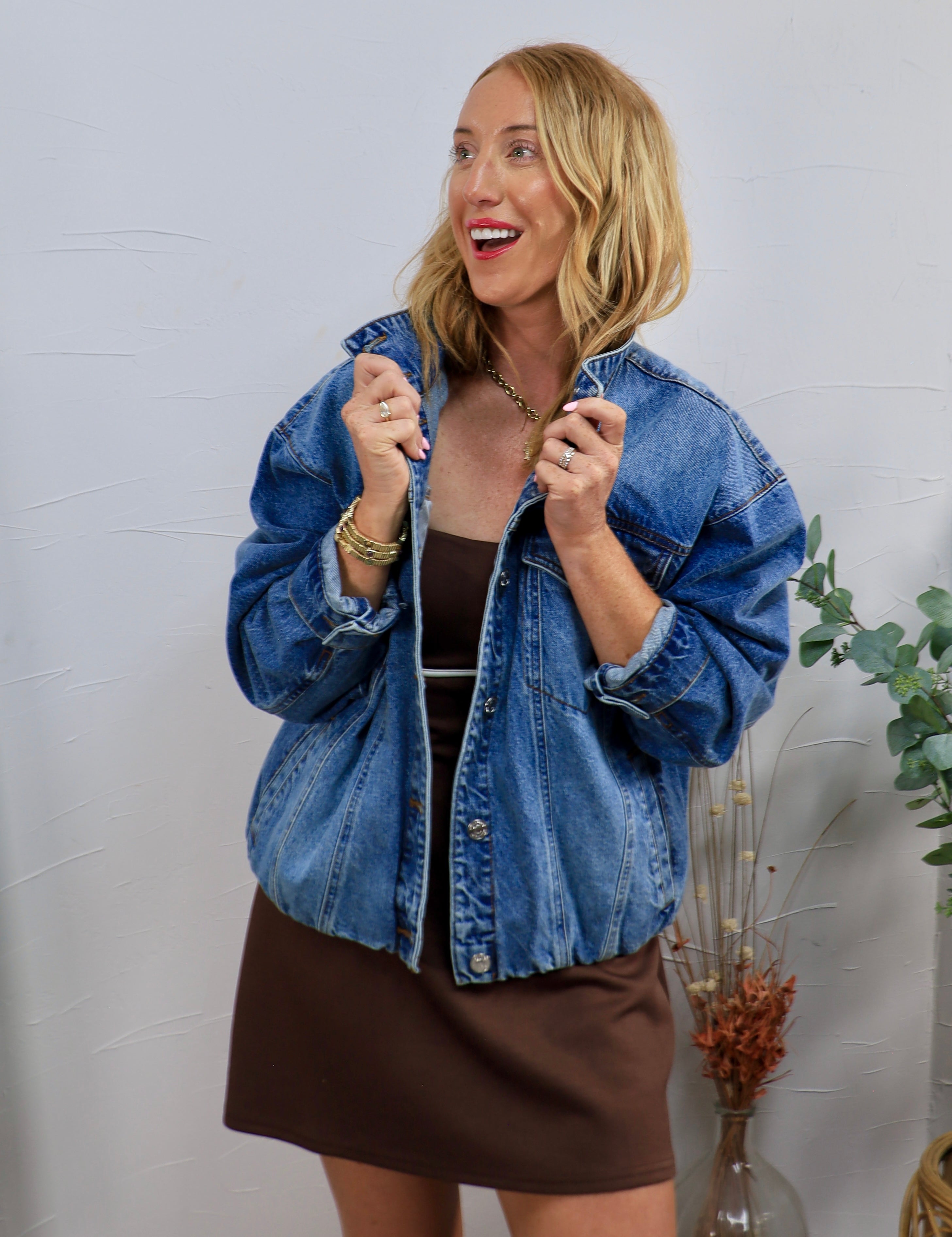 Woman wearing oversized medium wash denim jacket with snap buttons over a brown mini dress