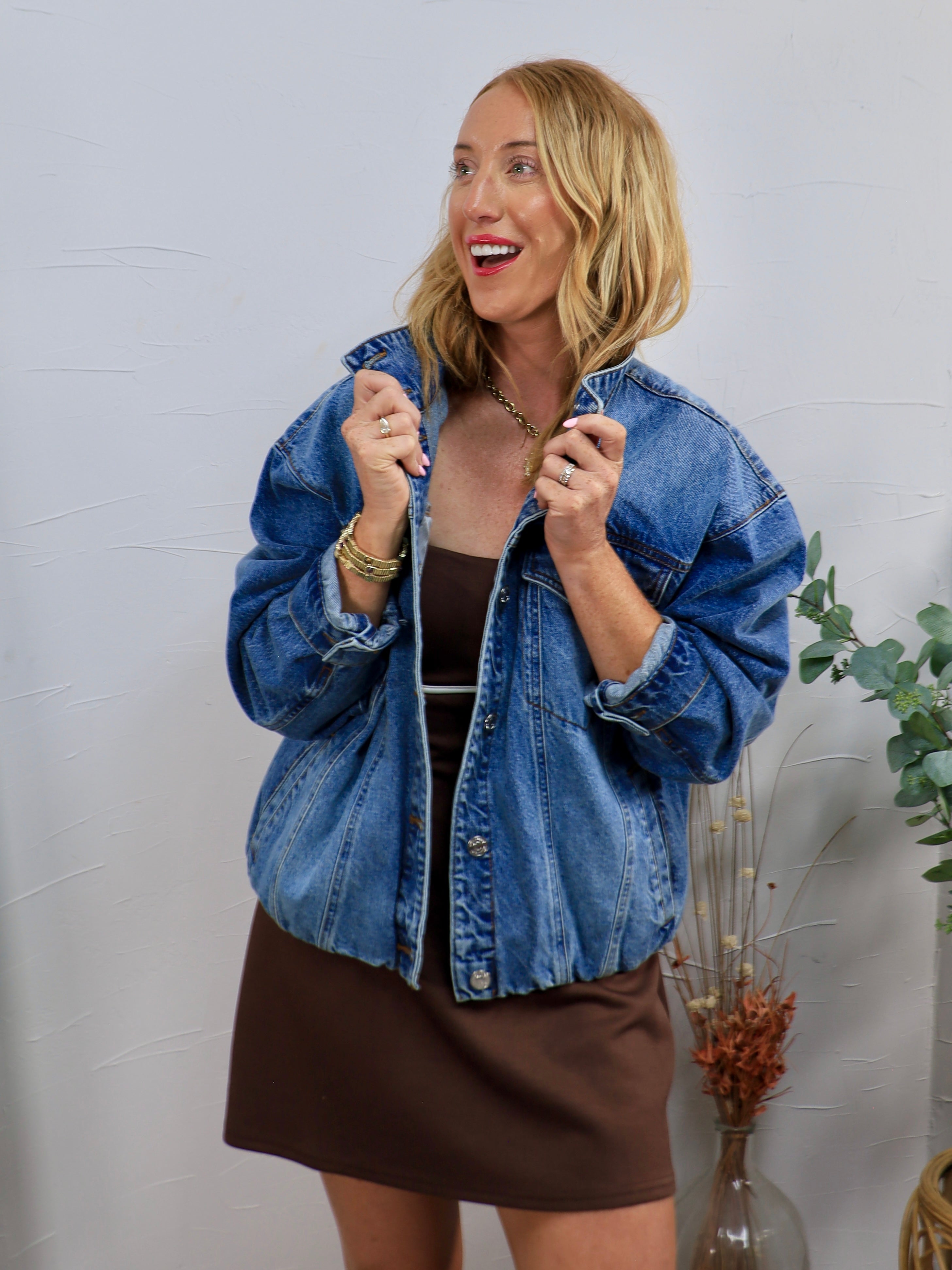 Woman wearing oversized medium wash denim jacket with snap buttons over a brown mini dress