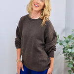 Oversized brown crewneck sweater styled with blue wide-leg jeans and a pearl necklace.