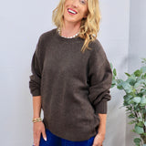 Oversized brown crewneck sweater styled with blue wide-leg jeans and a pearl necklace.