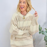 Woman wearing oversized cream and tan striped boucle V-neck sweater with blue velvet pants