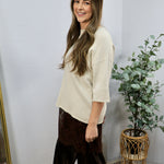 Cream knit short sleeve top with relaxed fit, styled with dark brown velvet wide-leg trousers.