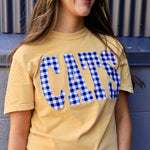 Woman wearing a butter yellow tee with blue gingham CATS applique lettering, smiling outdoors
