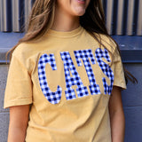 Woman wearing a butter yellow tee with blue gingham CATS applique lettering, smiling outdoors