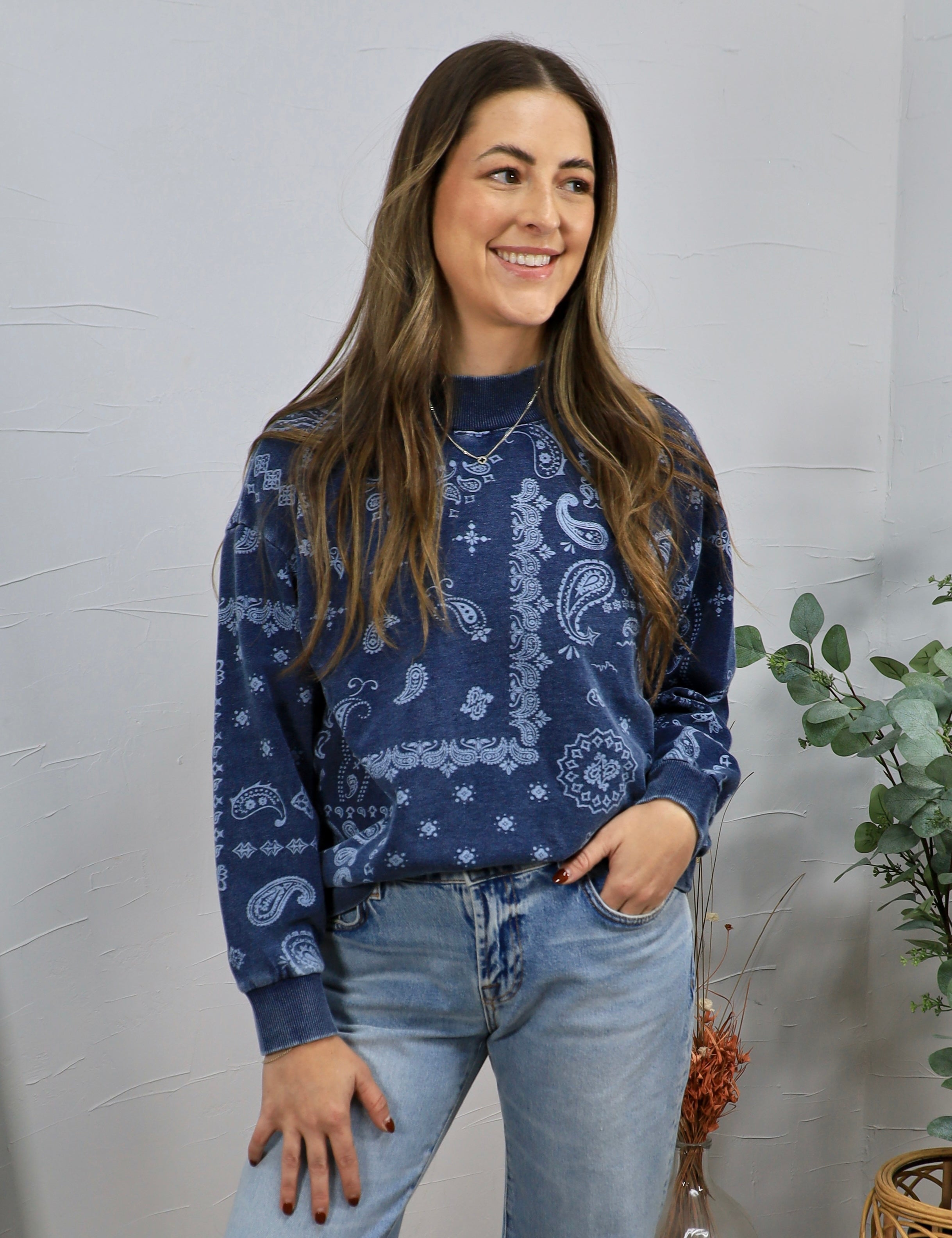 Woman wearing navy blue paisley print crewneck sweatshirt with light wash jeans, smiling