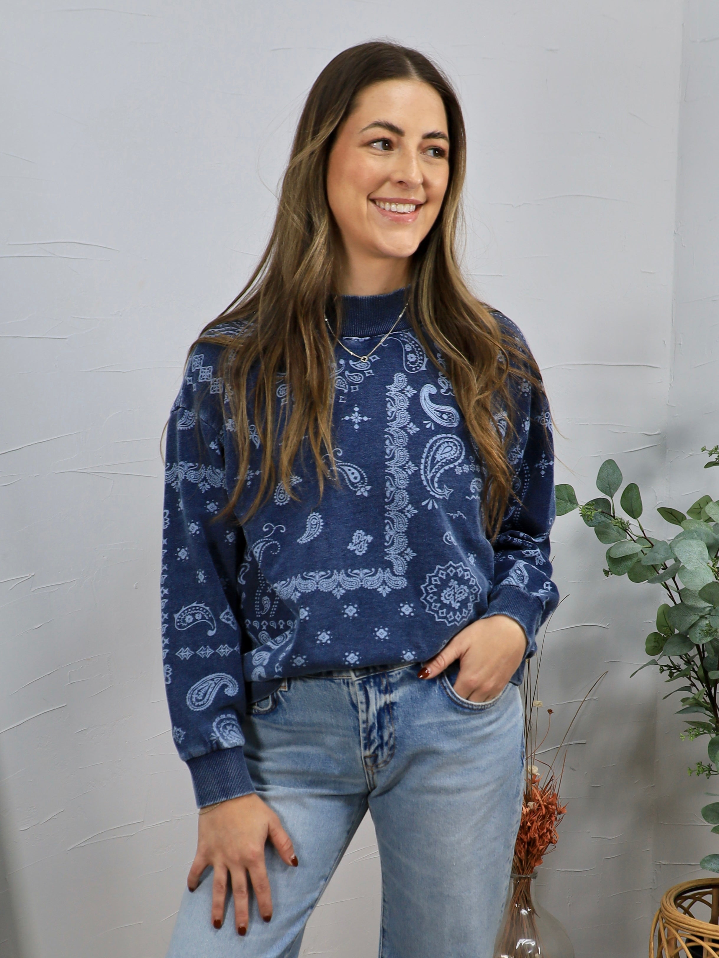 Woman wearing navy blue paisley print crewneck sweatshirt with light wash jeans, smiling