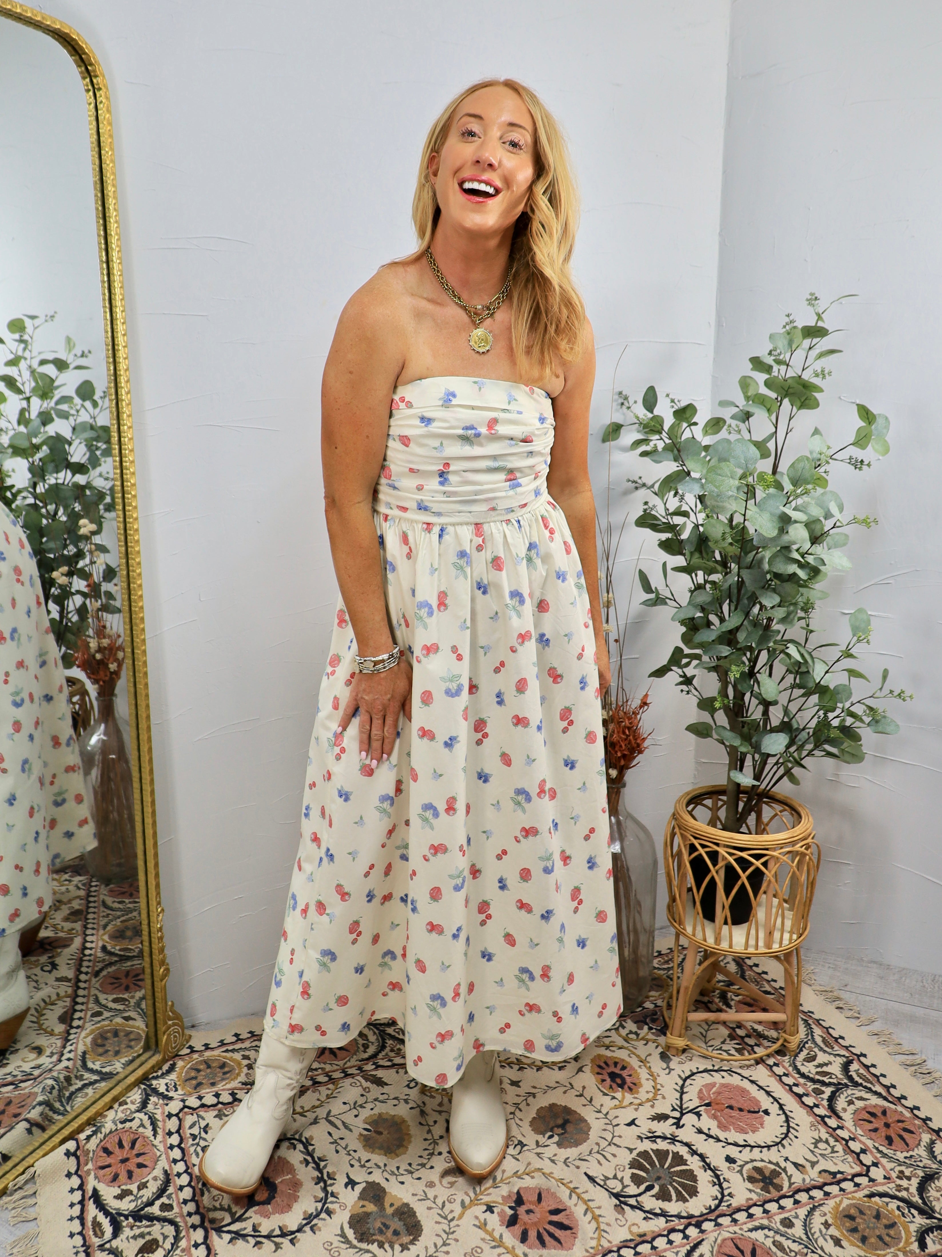 Woman wearing cream strapless midi dress with colorful floral print, styled with white boots and gold jewelry in boho setting