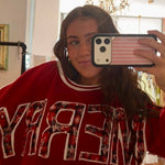 Red "MERRY" crewneck sweatshirt with plaid lettering and white trim, styled oversized in mirror selfie.