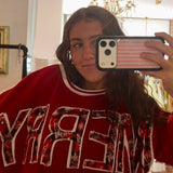 Red "MERRY" crewneck sweatshirt with plaid lettering and white trim, styled oversized in mirror selfie.
