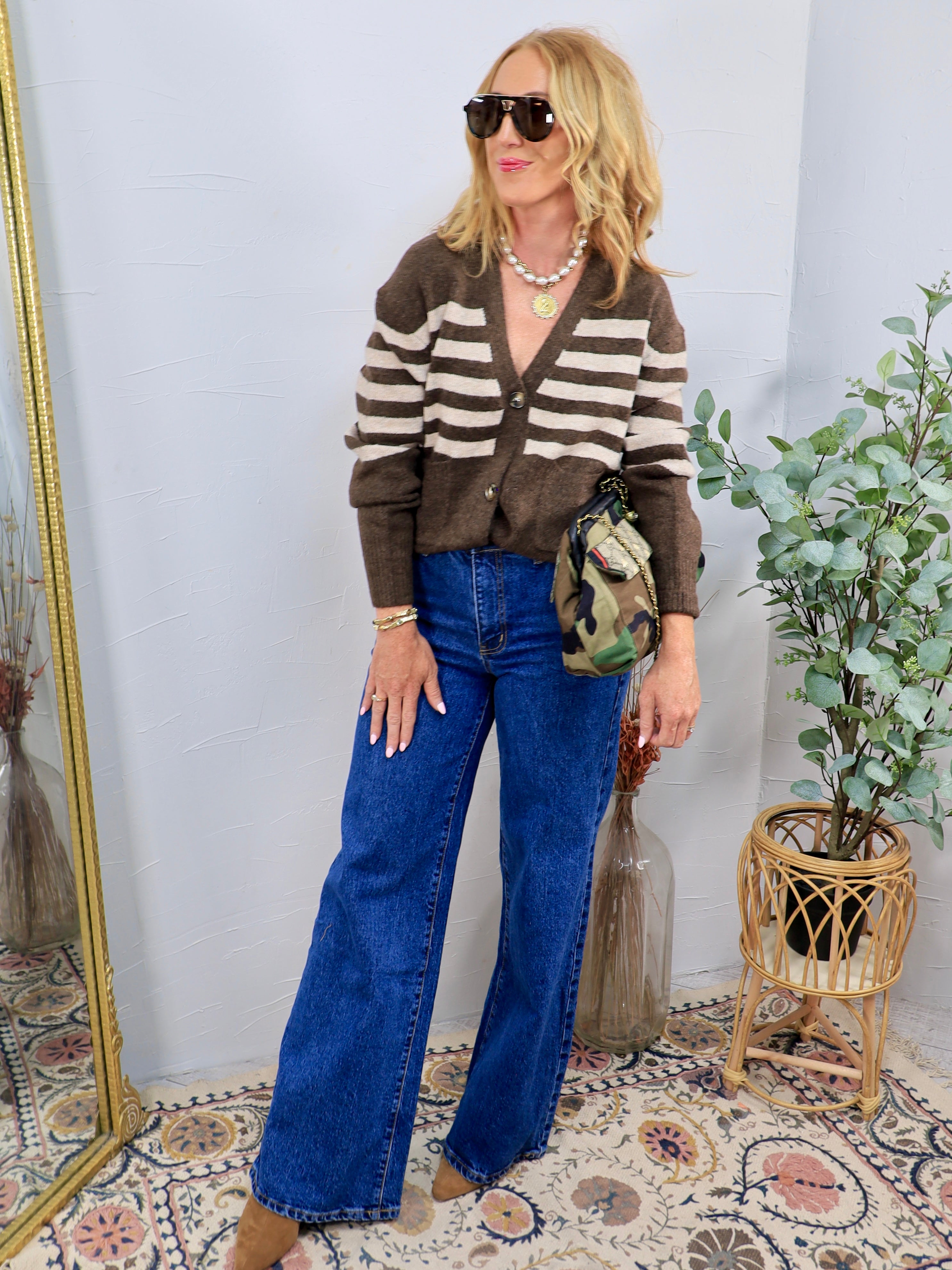 Wide leg dark wash blue denim jeans styled with a brown striped cardigan and suede boots.