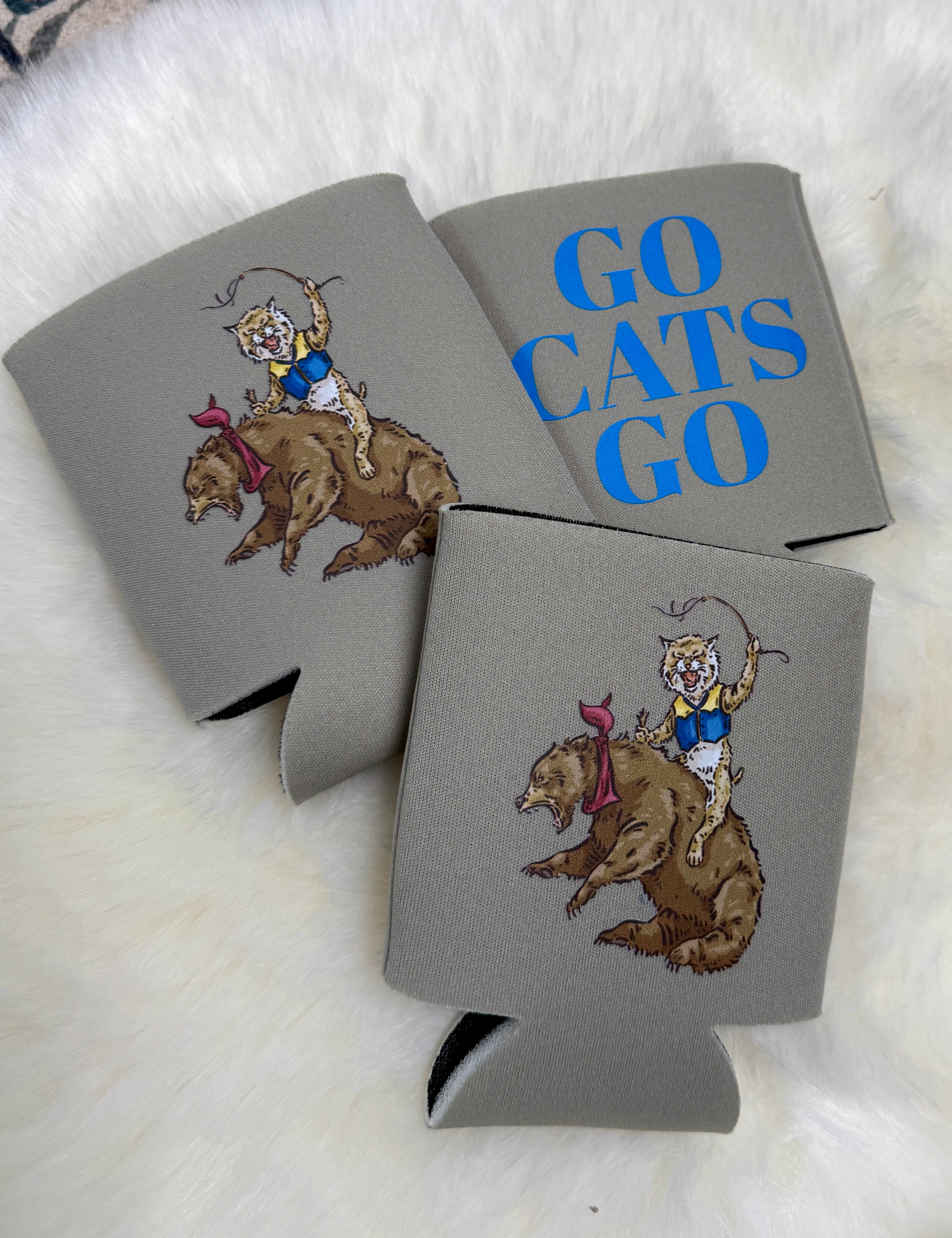 Gray foam koozies with wildcat riding bear illustration and blue Go Cats Go text on fur background