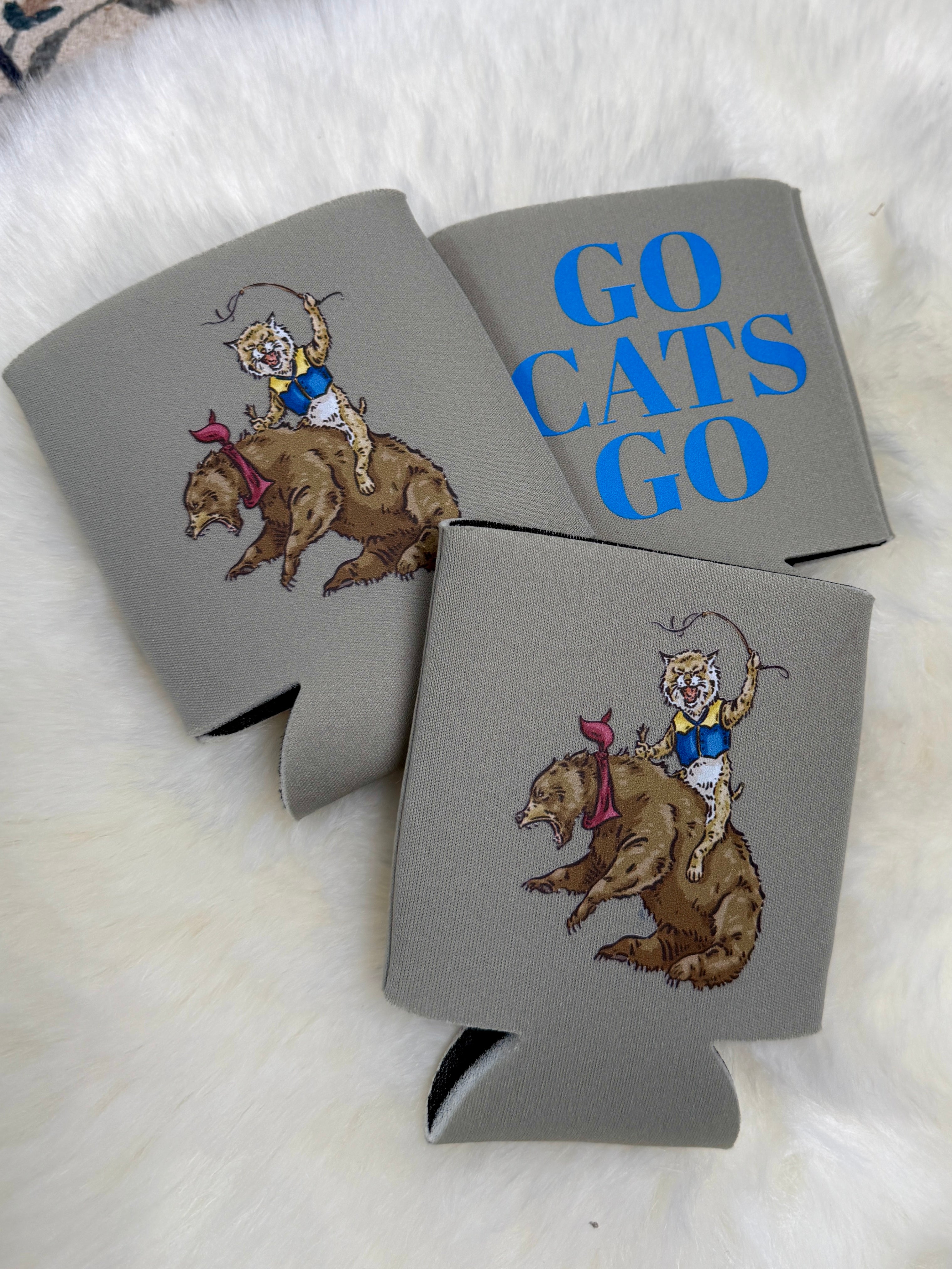 Gray foam koozies with wildcat riding bear illustration and blue Go Cats Go text on fur background