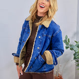 Blue denim jacket with tan sherpa teddy lining and collar, styled open over brown turtleneck and wide-leg pants.