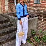 Woman wearing a blue and navy striped fitted button-front cardigan with white wide-leg pants and a woven crossbody bag