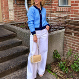 Woman wearing a blue and navy striped fitted button-front cardigan with white wide-leg pants and a woven crossbody bag