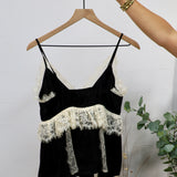 Black spaghetti strap camisole top with cream lace trim detailing at neckline and waist ruffle.