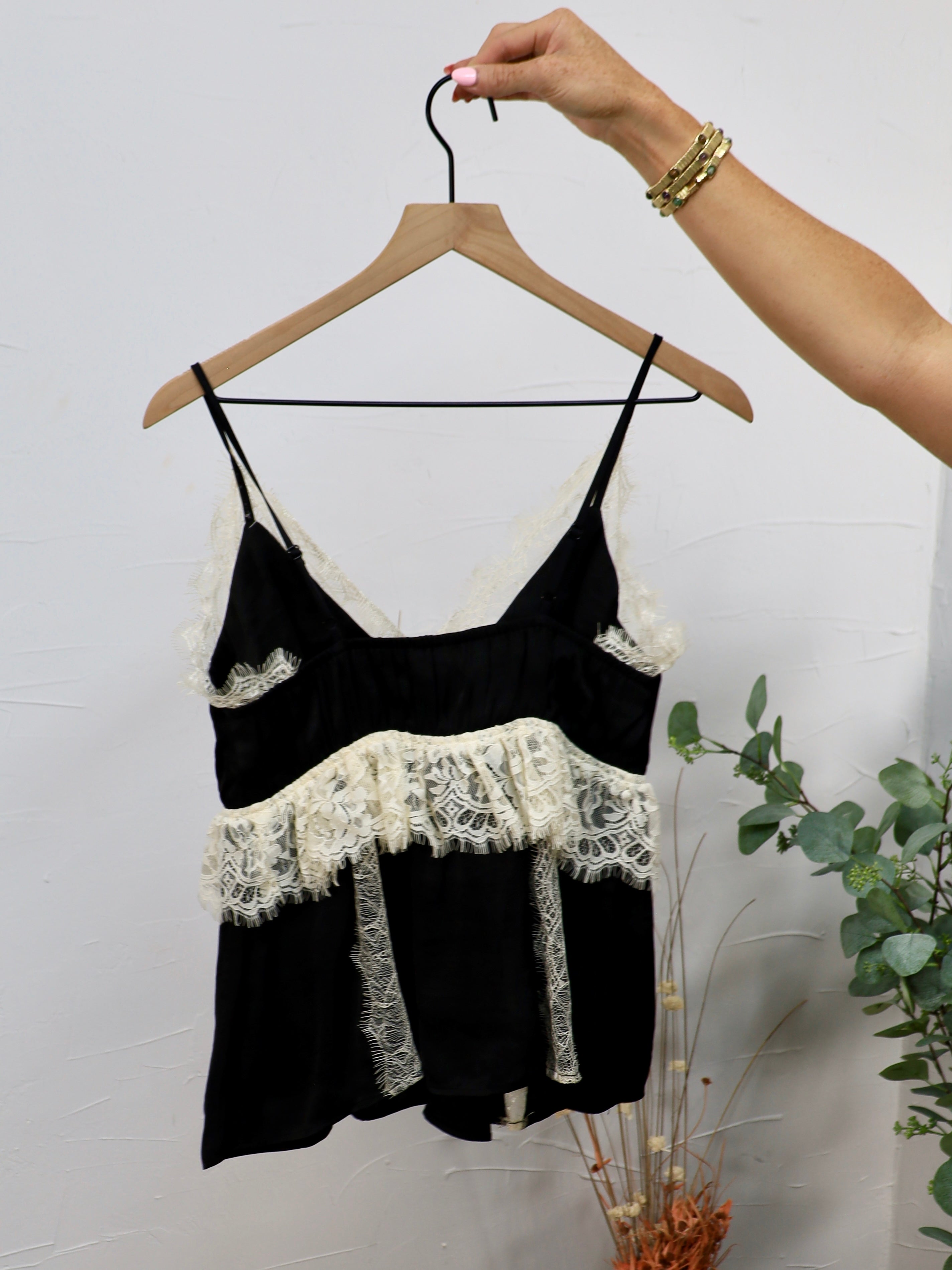 Black spaghetti strap camisole top with cream lace trim detailing at neckline and waist ruffle.