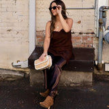 Woman wearing a chocolate brown lace cami with satin trousers and tan suede booties, seated outdoors