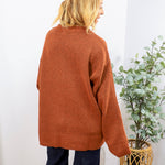 Rust orange oversized crewneck sweater shown from back, paired with dark navy wide-leg jeans.