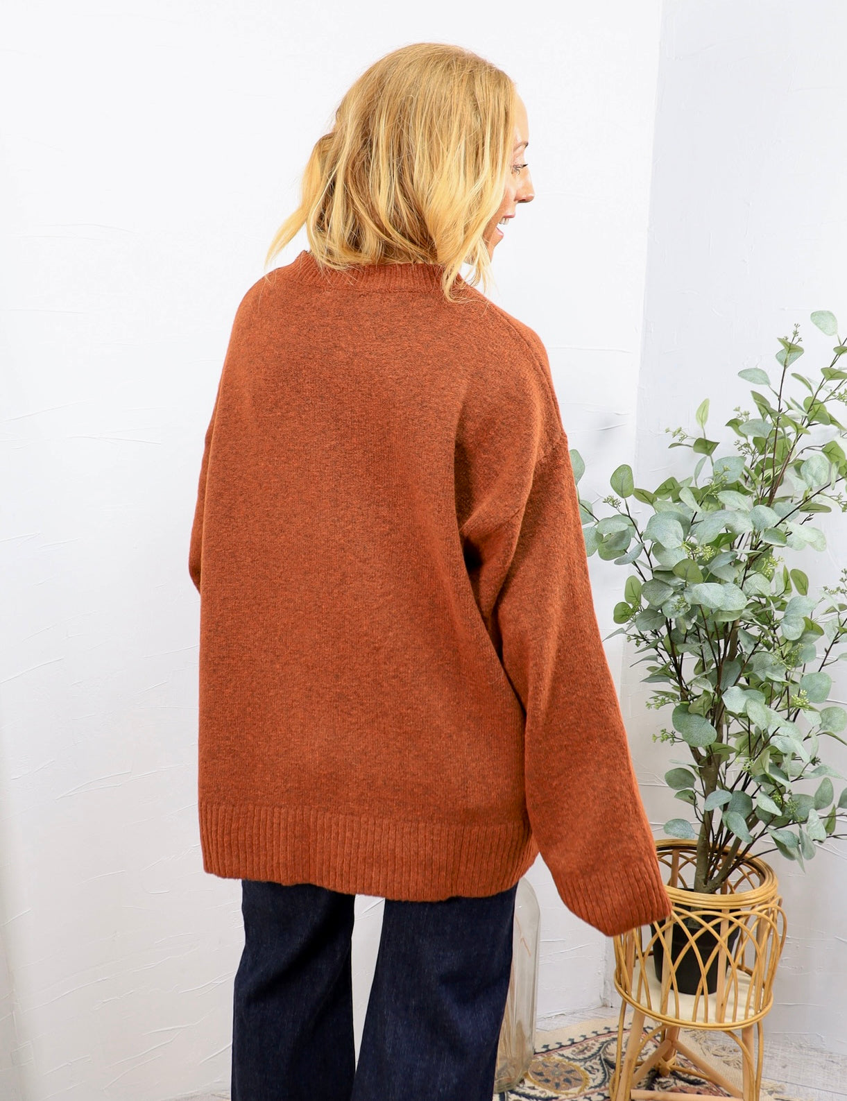 Rust orange oversized crewneck sweater shown from back, paired with dark navy wide-leg jeans.