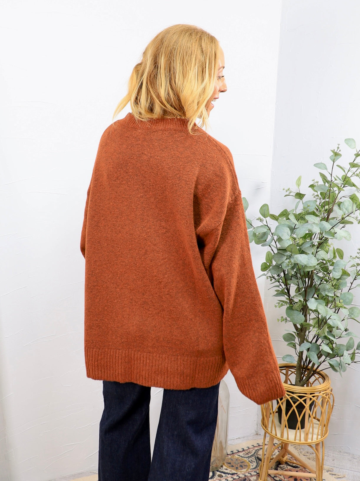 Rust orange oversized crewneck sweater shown from back, paired with dark navy wide-leg jeans.