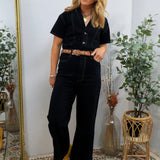 Woman wearing black short-sleeve denim coveralls with brown leather belt and yellow pointed-toe shoes, styled with layered ne