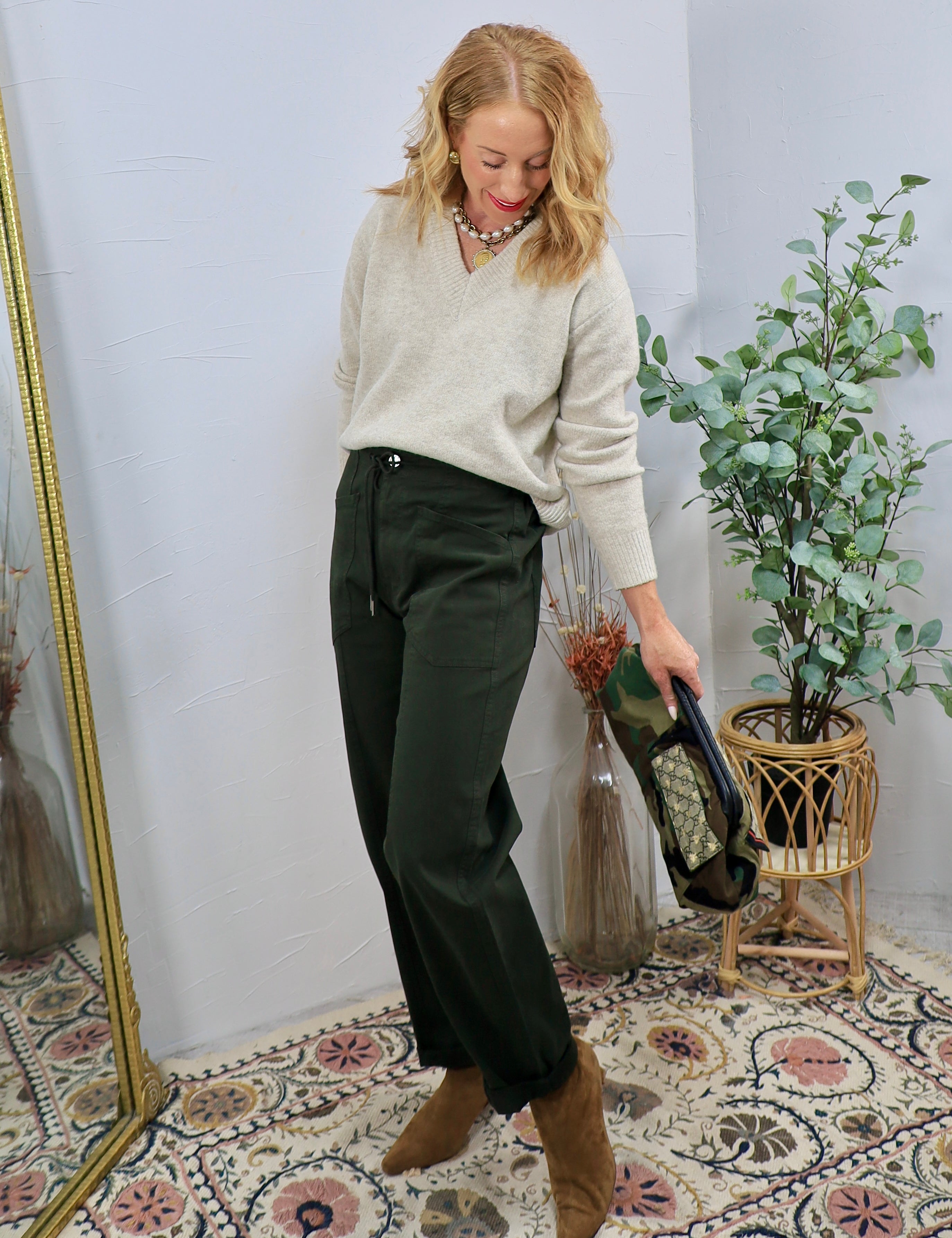 Dark green drawstring wide-leg trousers styled with cream v-neck sweater, tan ankle boots, and statement necklace.