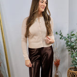 Woman wearing a cropped oatmeal button-down cardigan with brown satin wide-leg trousers