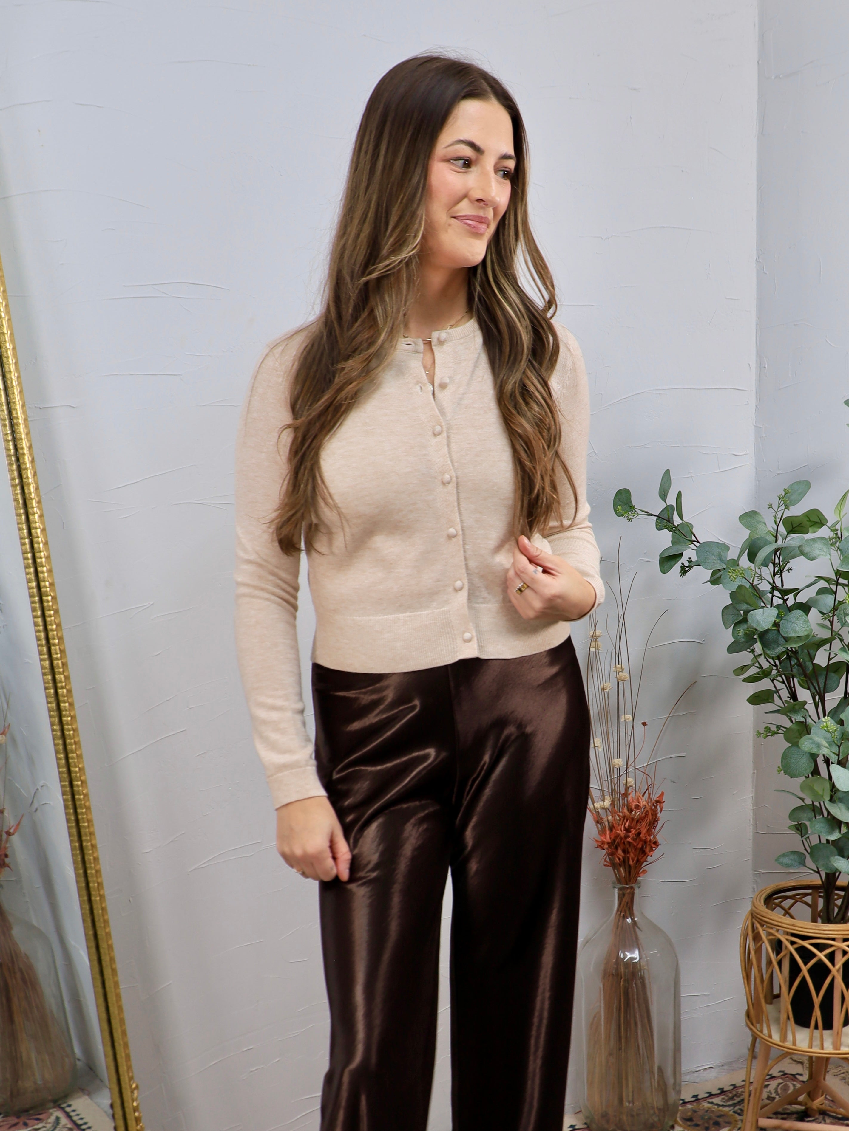 Woman wearing a cropped oatmeal button-down cardigan with brown satin wide-leg trousers
