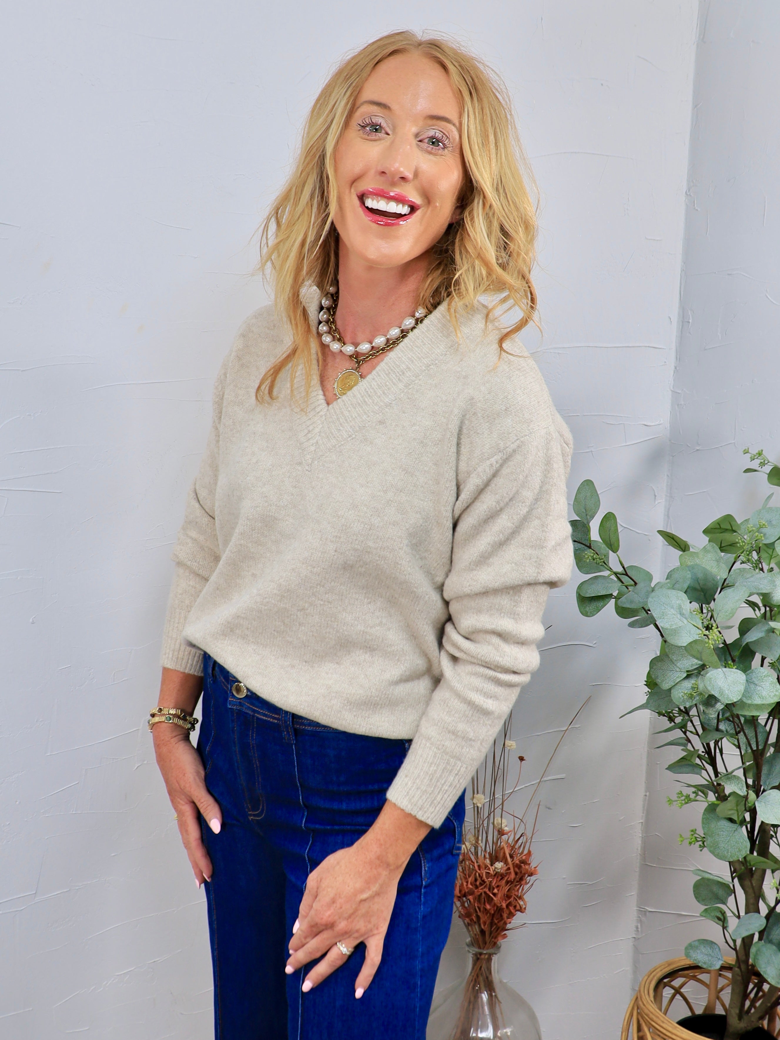 Oatmeal beige V-neck knit sweater styled with dark blue jeans and layered pearl chain necklace.