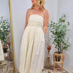 Cream strapless midi dress with ruched bodice and full gathered skirt, styled with platform sandals.