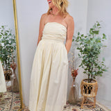 Cream strapless midi dress with ruched bodice and full gathered skirt, styled with platform sandals.