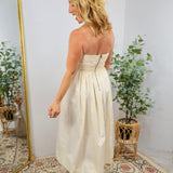 Cream strapless midi dress with ruched bodice and full skirt, back zipper closure, styled with bow heels.