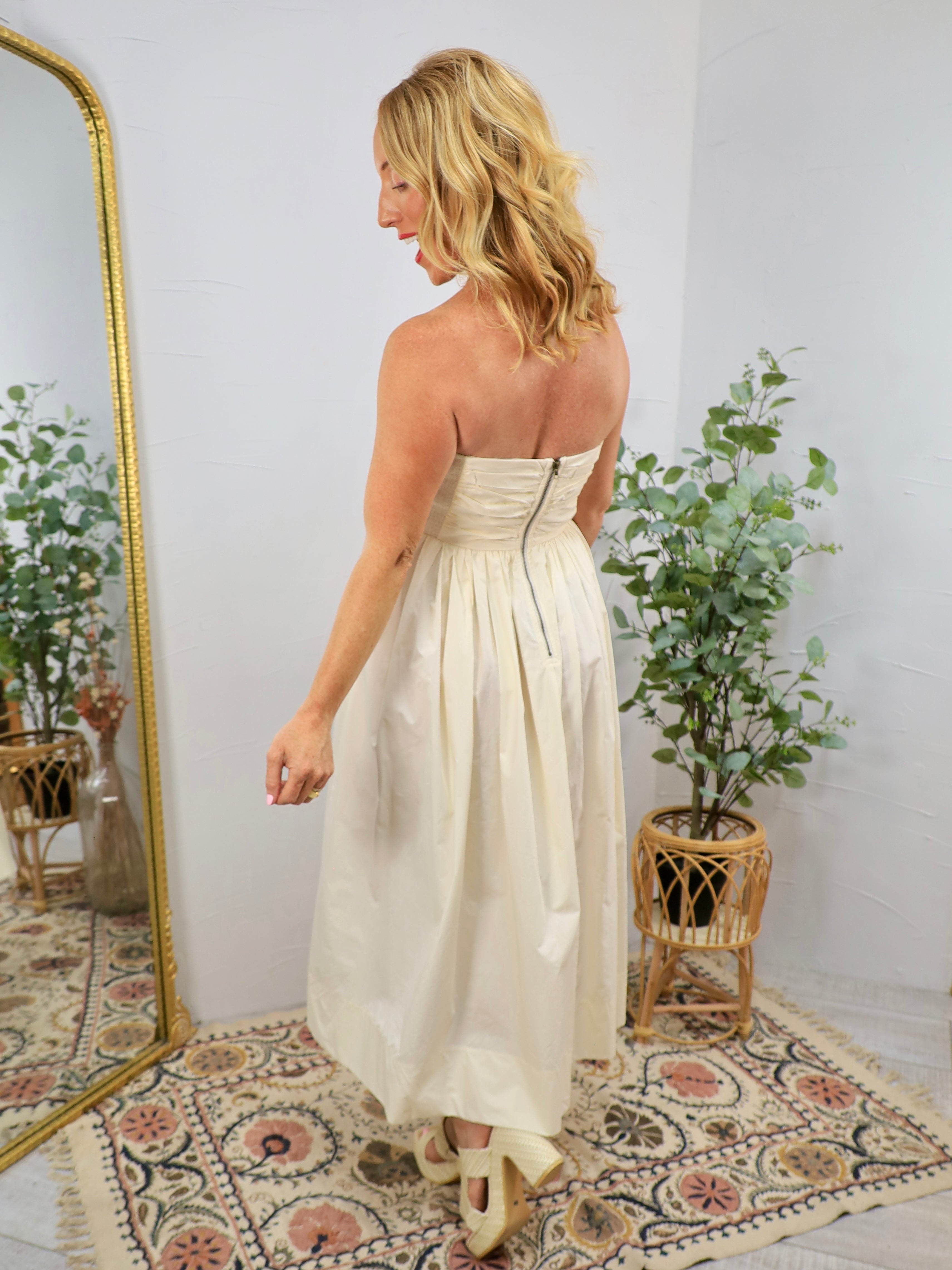 Cream strapless midi dress with ruched bodice and full skirt, back zipper closure, styled with bow heels.
