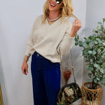 Woman wearing oatmeal V-neck oversized knit sweater with wide-leg dark denim jeans and layered gold jewelry