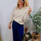Woman wearing oatmeal V-neck oversized knit sweater with wide-leg dark denim jeans and layered gold jewelry