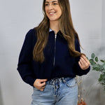 Navy blue zip-up cropped cardigan styled over a striped shirt with light wash jeans.
