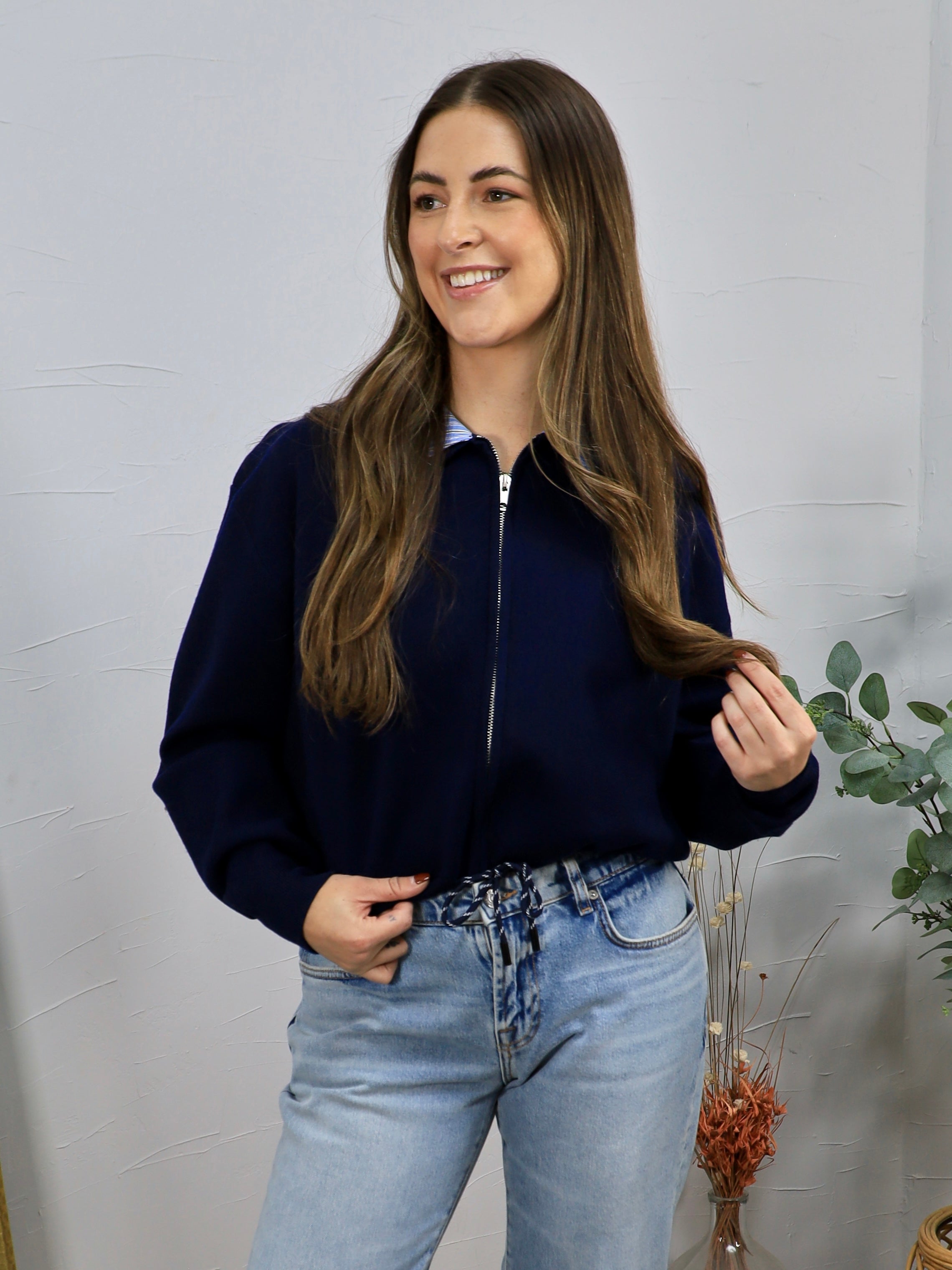Navy blue zip-up cropped cardigan styled over a striped shirt with light wash jeans.