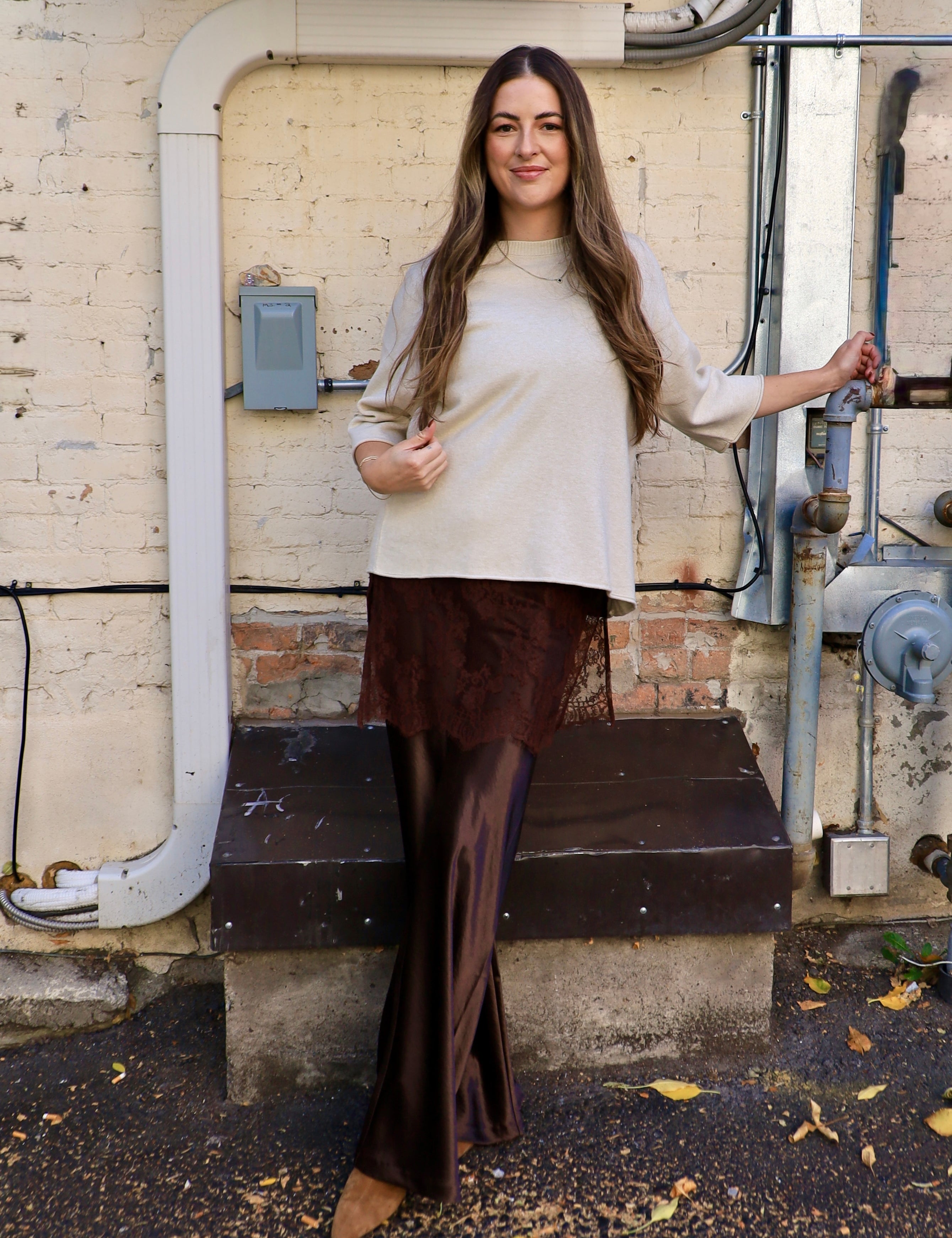 Woman wearing cropped oatmeal sweater top with bell sleeves and lace hem detail