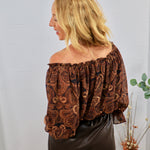 Brown and black paisley off-shoulder blouse with voluminous sleeves, styled with dark faux leather pants.