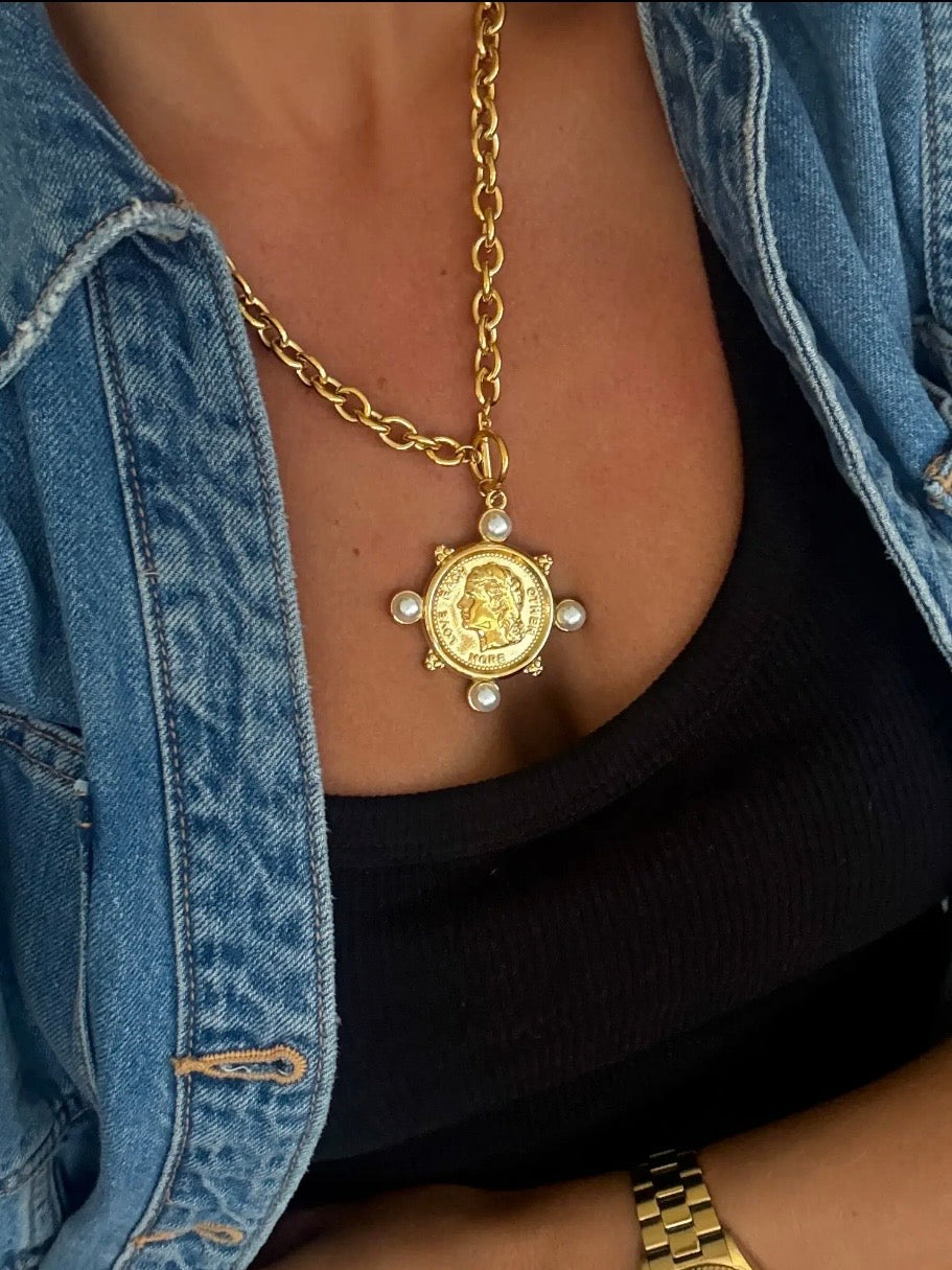 Gold coin pendant necklace with four pearl accents on chunky chain, styled with black top and denim jacket.