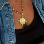 Gold coin pendant necklace with four pearl accents on chunky chain, styled with black top and denim jacket.