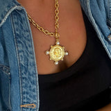 Gold coin pendant necklace with four pearl accents on chunky chain, styled with black top and denim jacket.